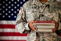 Military member holding textbooks in front of American flag