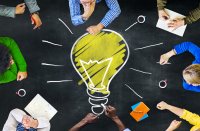 Group of people sitting around drawing of large light bulb