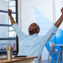 Attractive man with arms raised in success in front of laptop