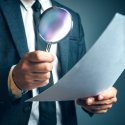 Man holding magnifying glass looking at paper