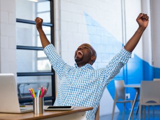 Attractive man with arms raised in success in front of laptop